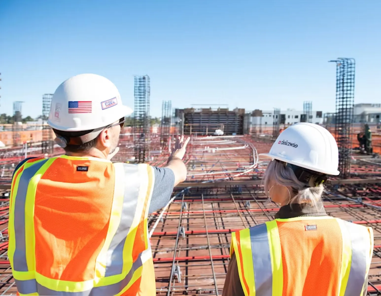 Two persons in orange vests who is pointing at a construction site.