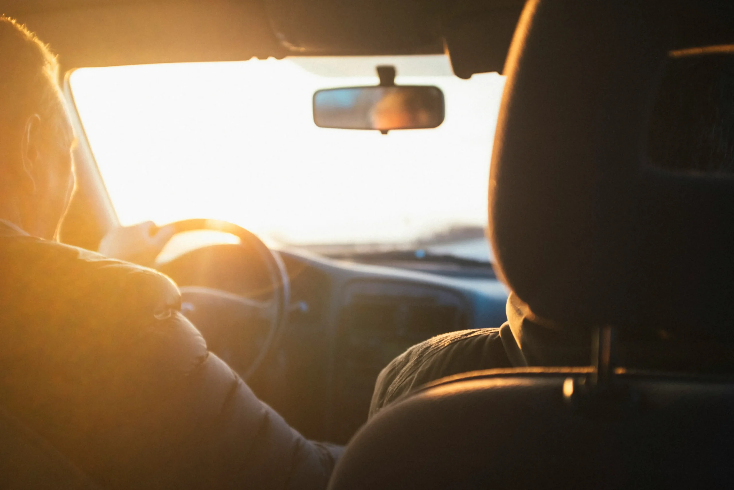 A photo from behind of a man driving a car in the sunset.