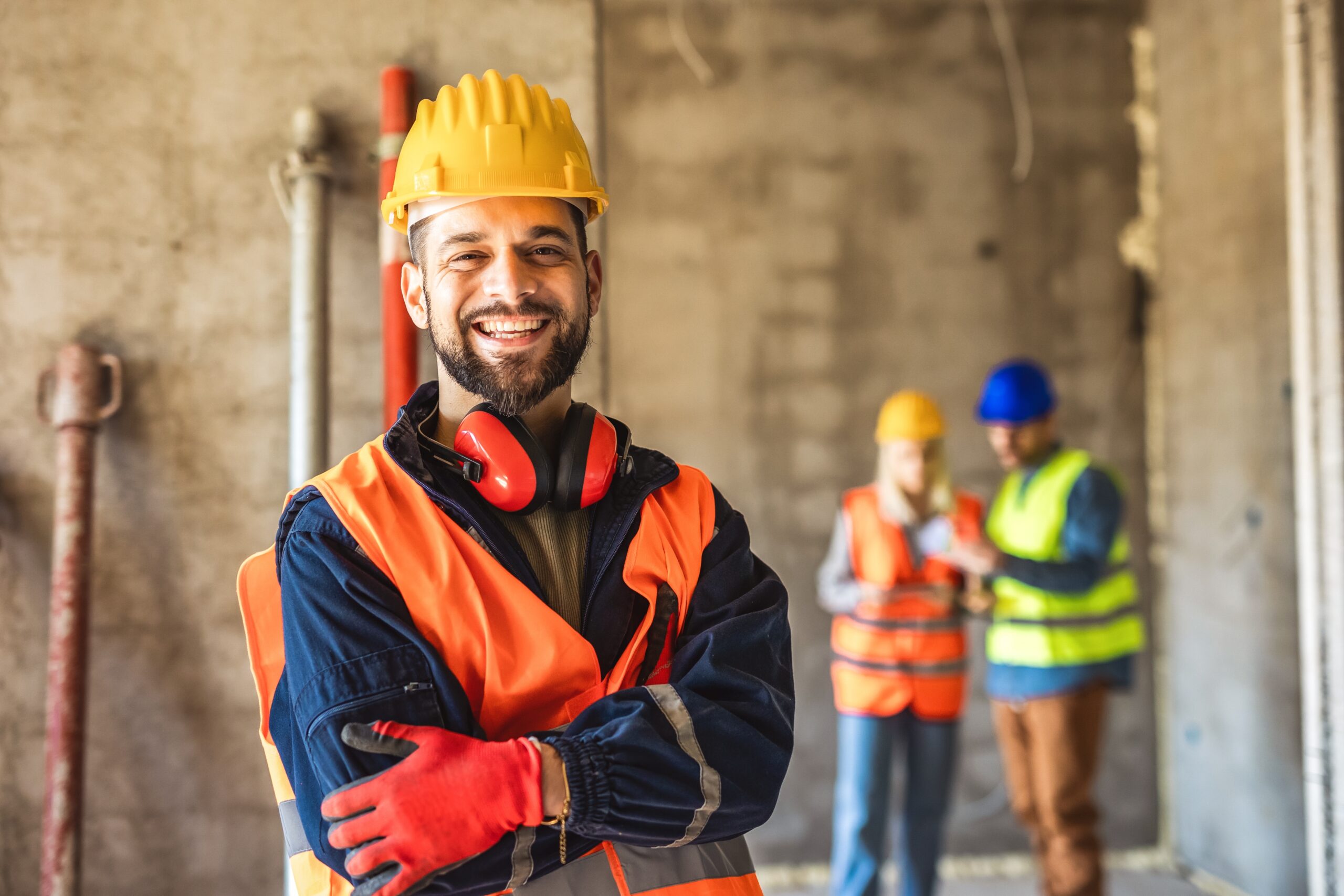 Worker in safety gear smiling with colleagues working behind them