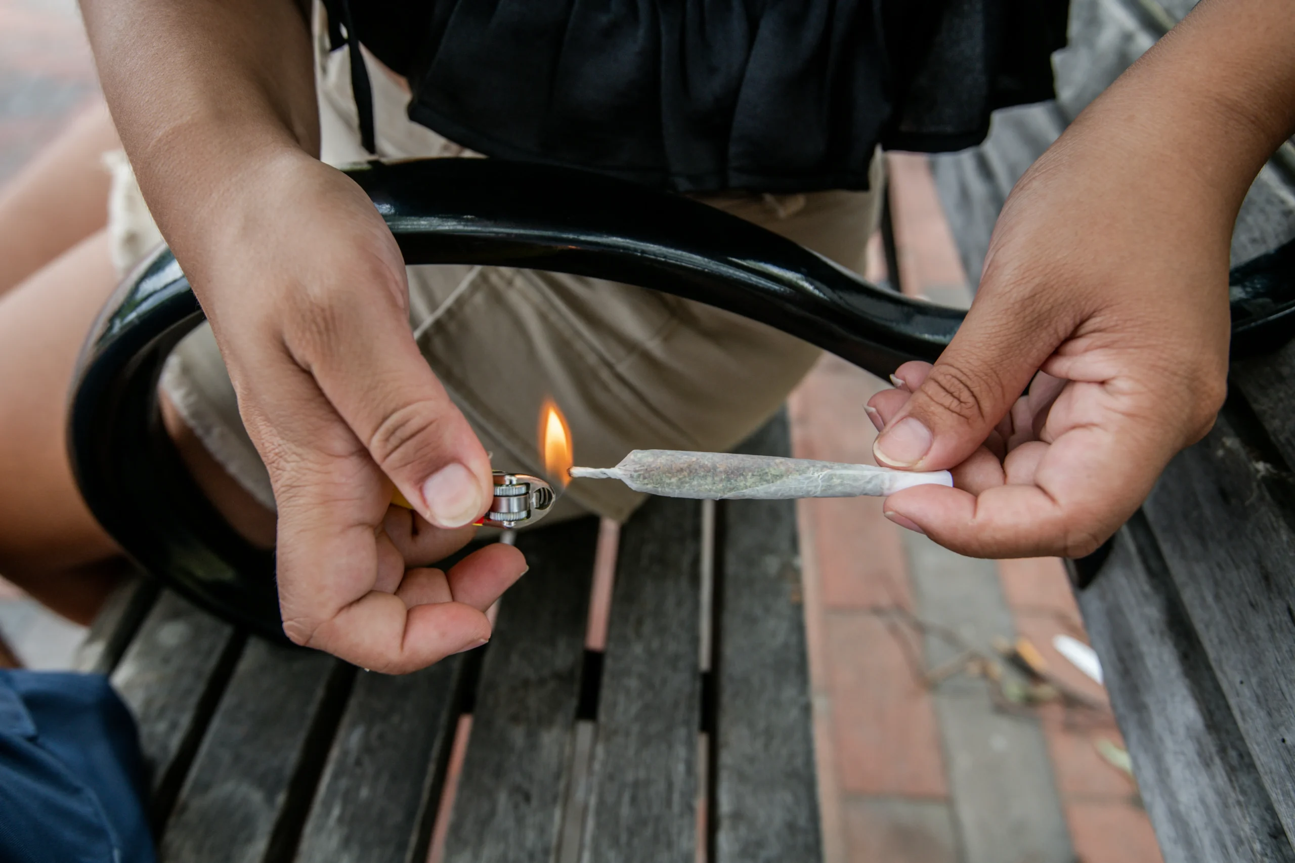 Man lighting marijuana joint on a park bench